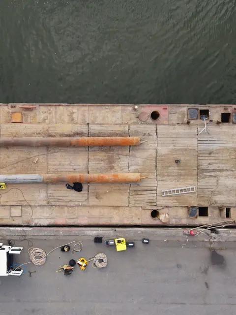 Drone view from above of a work pontoon moored along a harbour quay, inspection equipment laid out on the quay